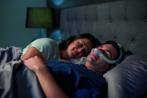 Couple sleeping in bed while man wears CPAP mask