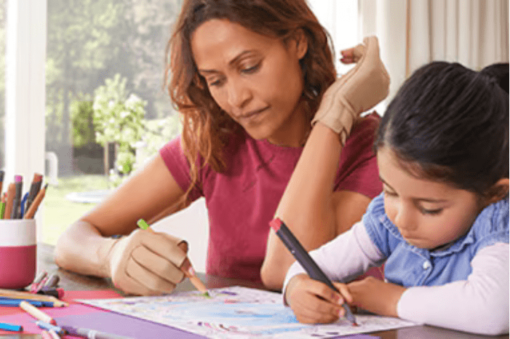 woman coloring with a little girl. the woman is wearing two actimove arthritis gloves