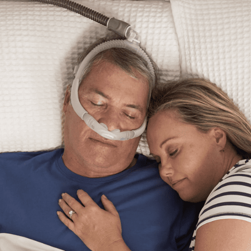 man and woman snuggling in bed, he is wearing a nasal cpap mask