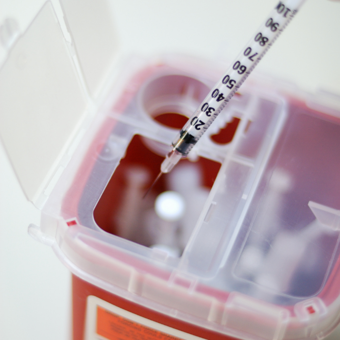 insulin needle going into a sharps container for disposal
