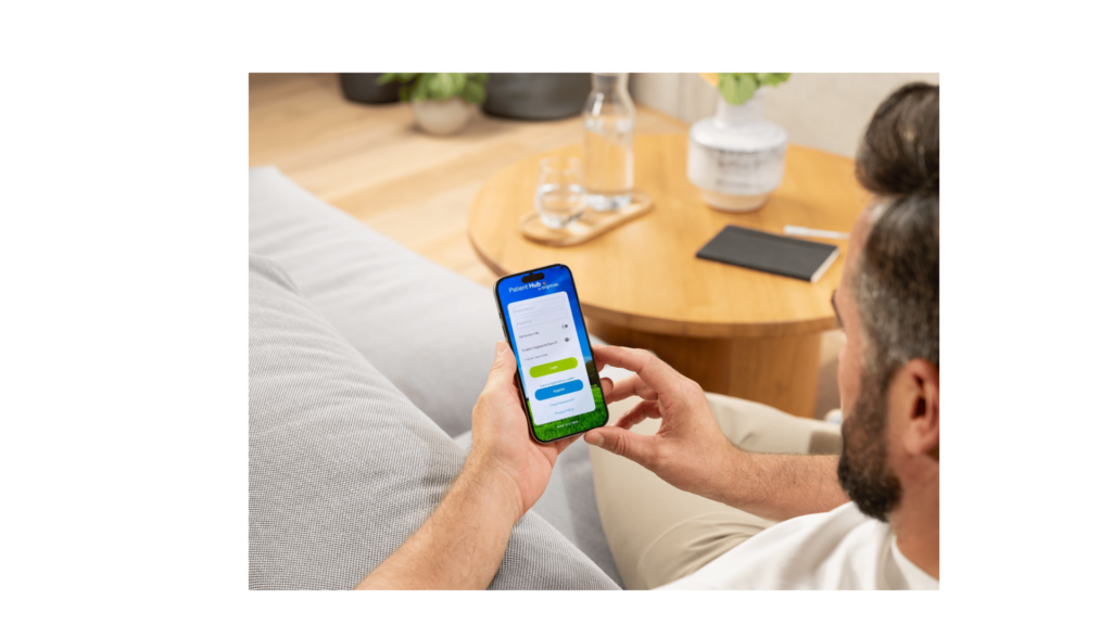 View over a man's shoulder as he's on a phone displaying Patient Hub while sitting on a couch